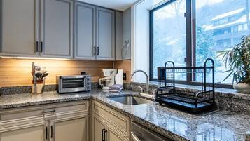 A kitchen with granite countertops, stainless steel appliances, and a large window with a view of a snowy landscape.