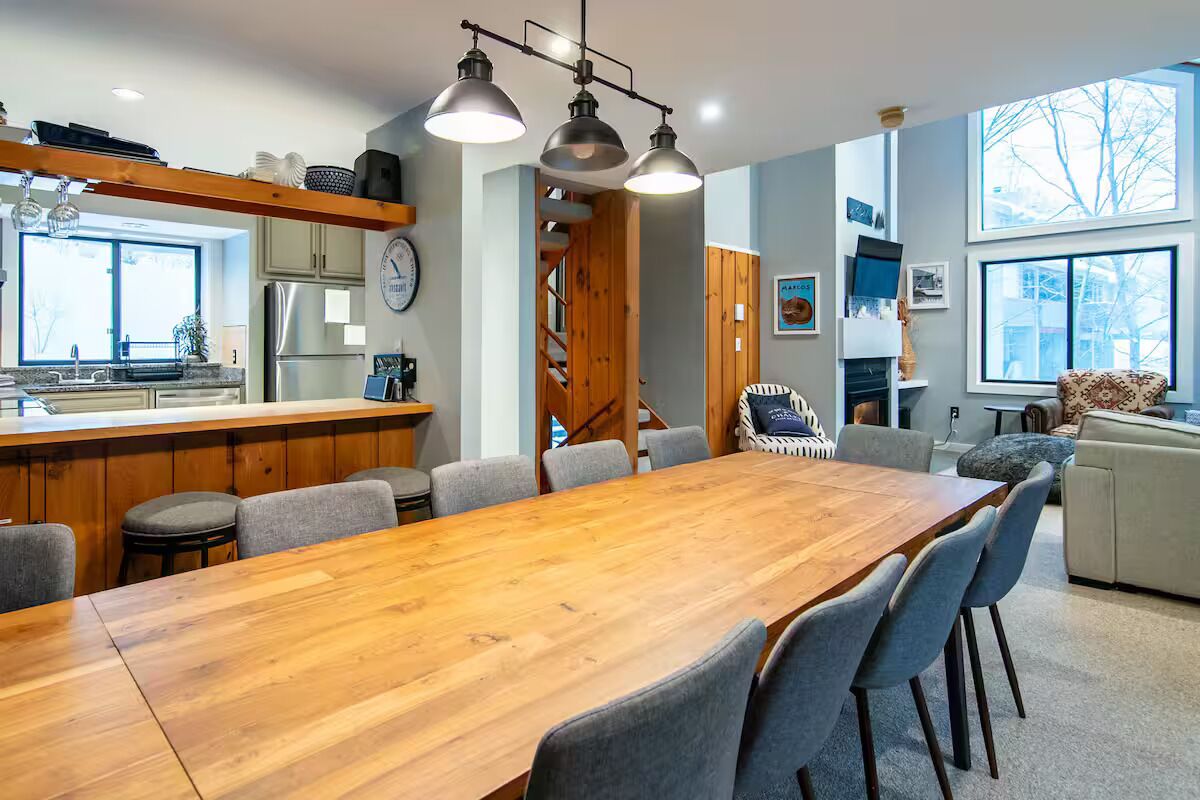 Una cucina moderna con isola in legno, zona pranzo con tavolo e sedie di grandi dimensioni, e un'area salotto accogliente con divano e poltrone.