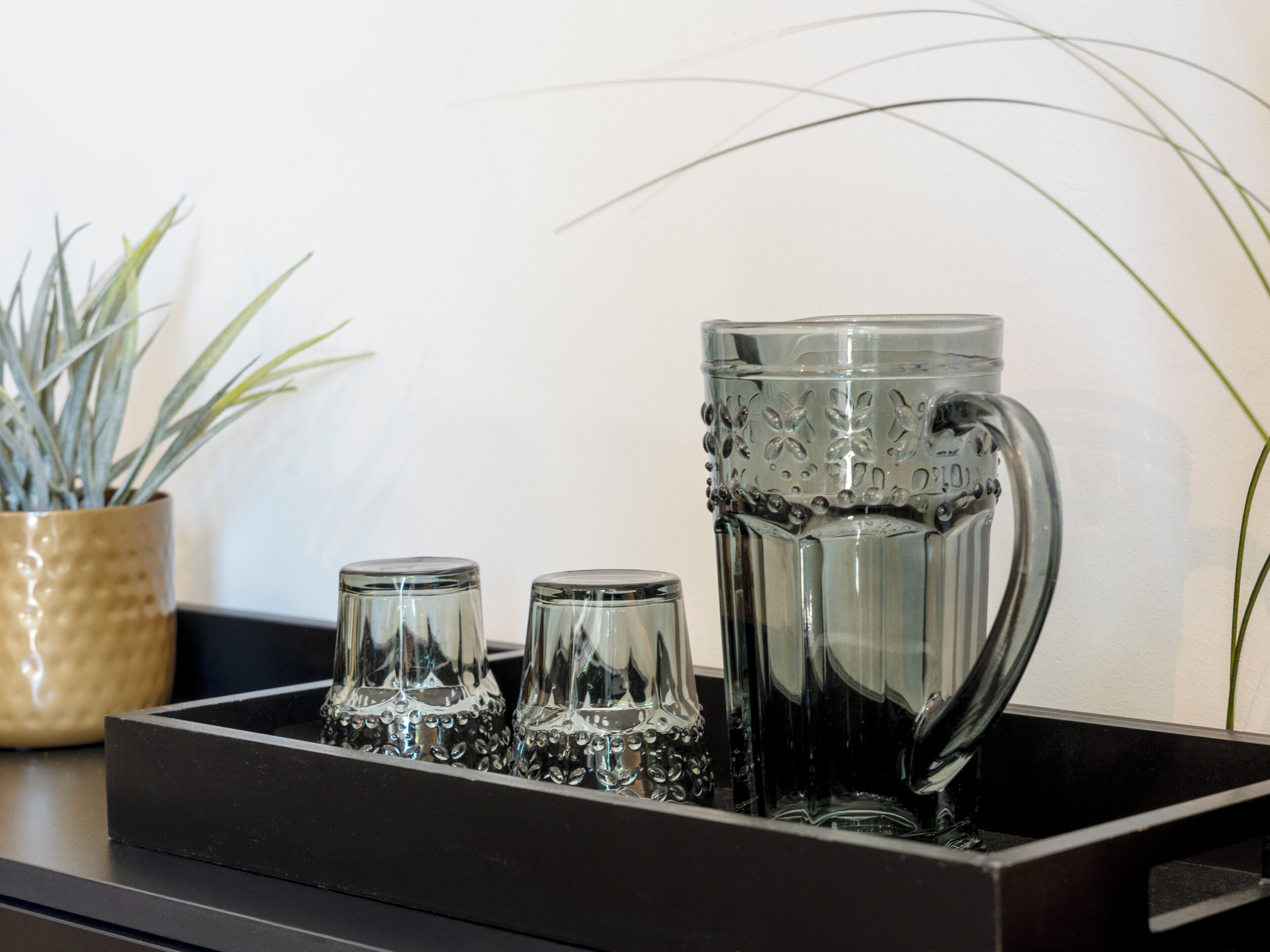 A tray with a large glass pitcher and three smaller glasses, likely for serving beverages.
