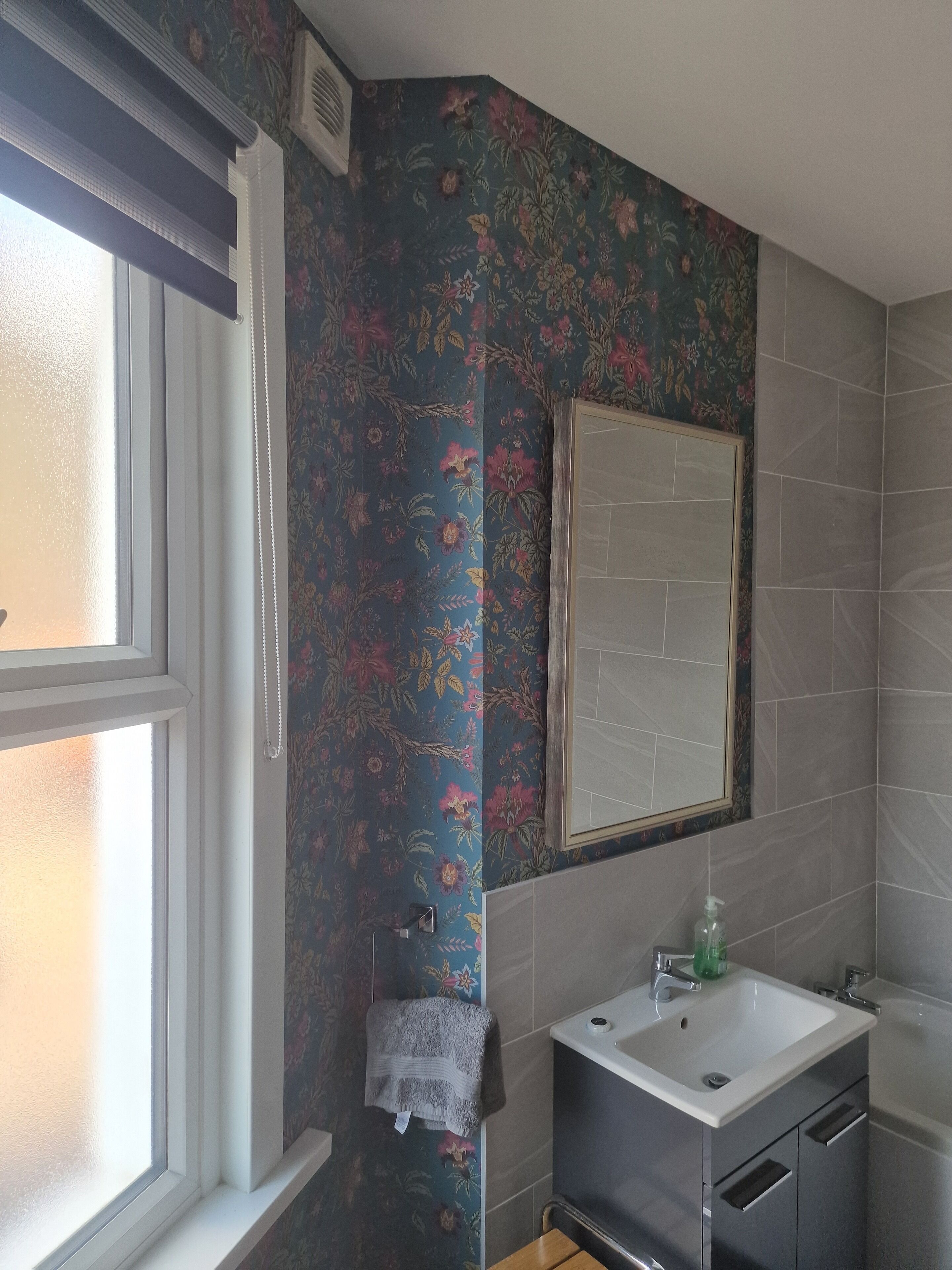 A bathroom with floral wallpaper, a mirror, a sink, and a shower.