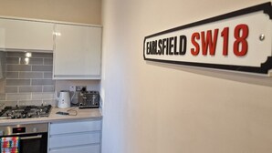 Eine Küche mit weißen Schränken, einem Herd und einem Toaster. Ein Schild an der Wand zeigt 'EARLSFIELD SW18'.