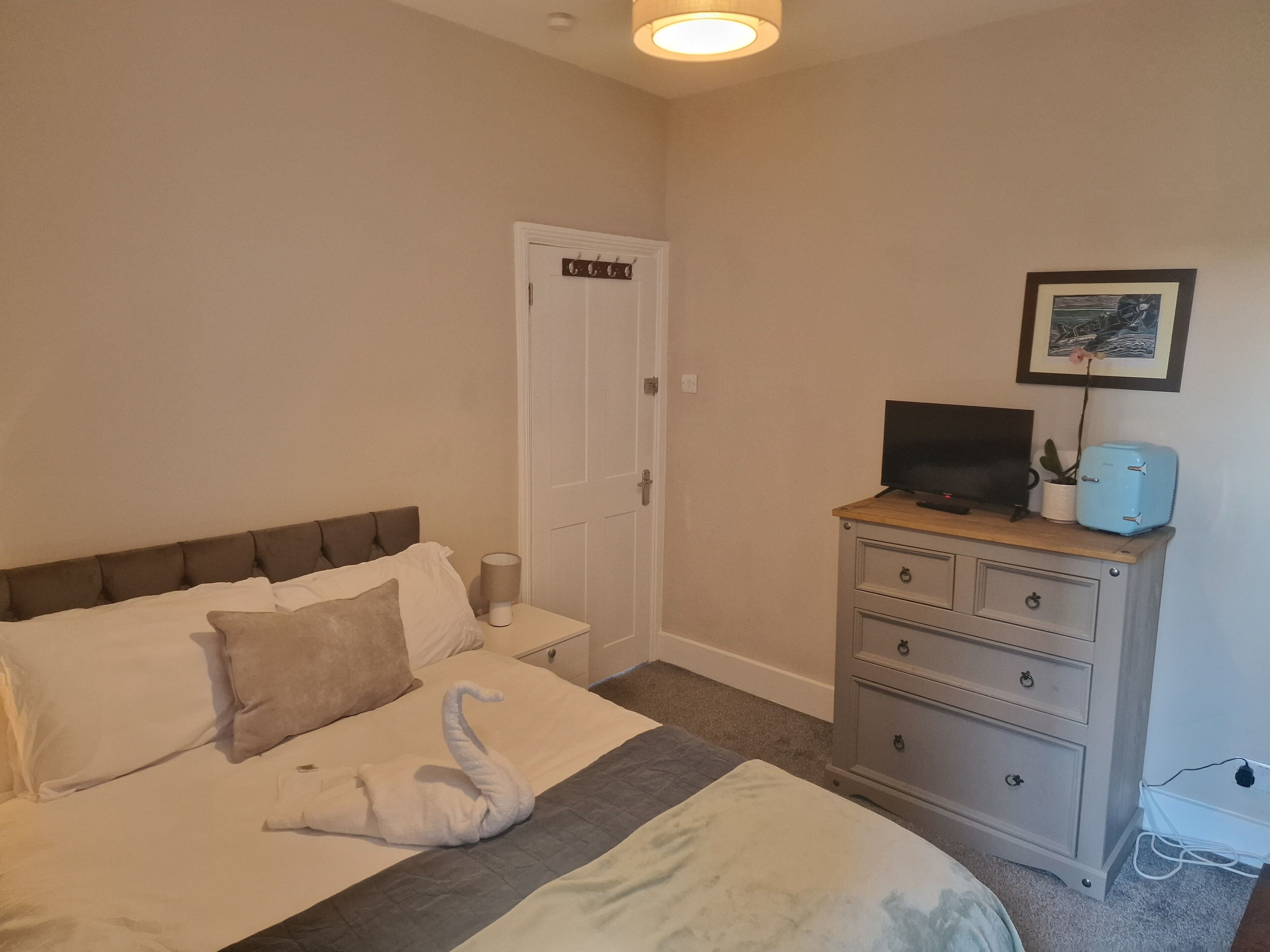 Un dormitorio con cama, cómoda, televisor y puerta.