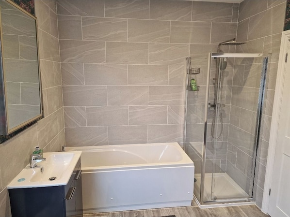 A modern bathroom with a bathtub, a glass-enclosed shower, and a sink with a mirror.