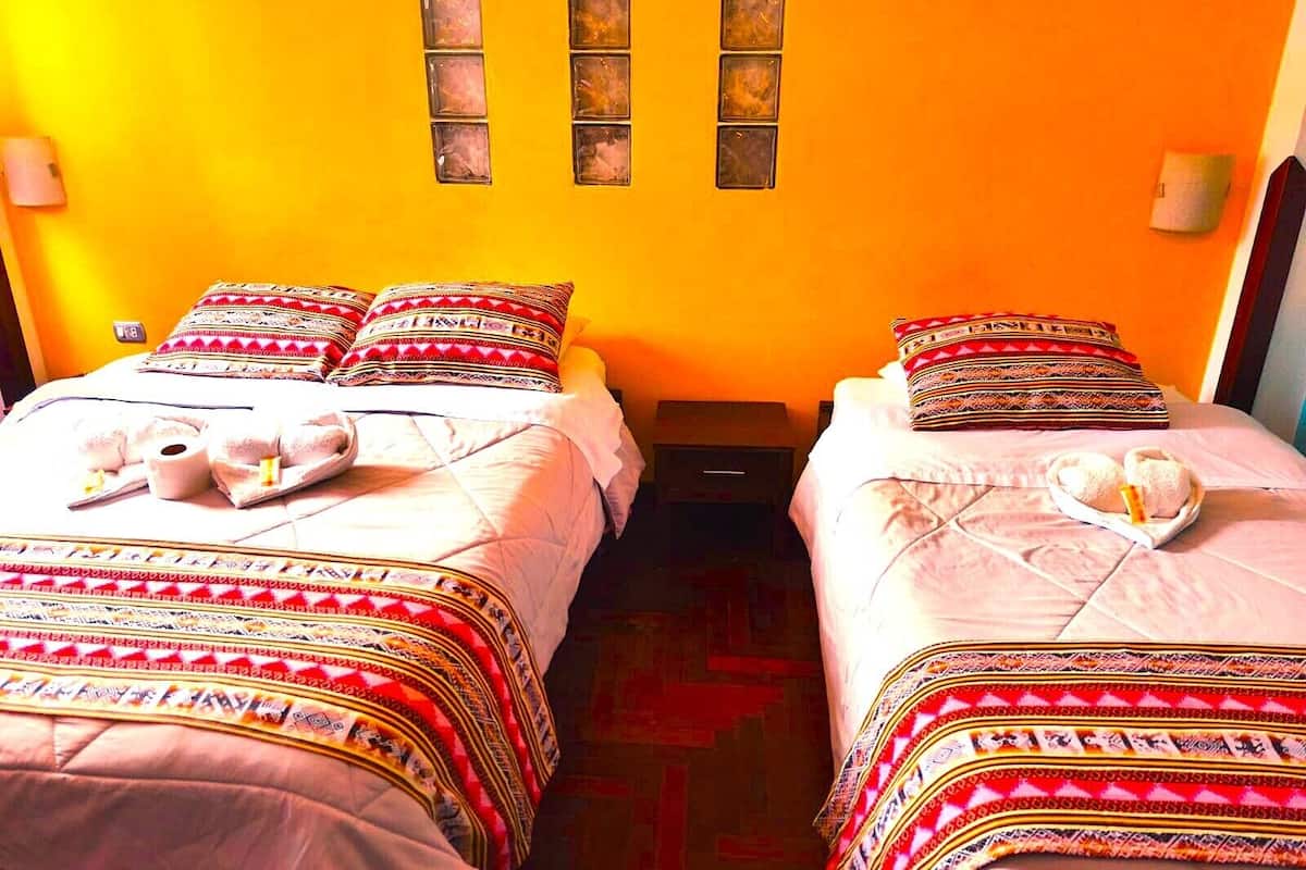 Une chambre d’hôtel avec deux lits, chacun agrémenté de draps et d’oreillers à motifs, une petite table de chevet et un luminaire fixé au mur.