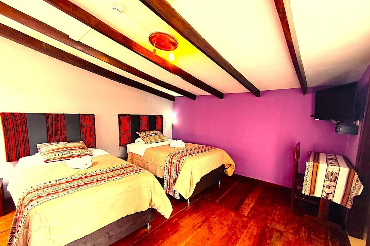 Une chambre avec deux lits, des poutres en bois, un mur violet et un téléviseur.