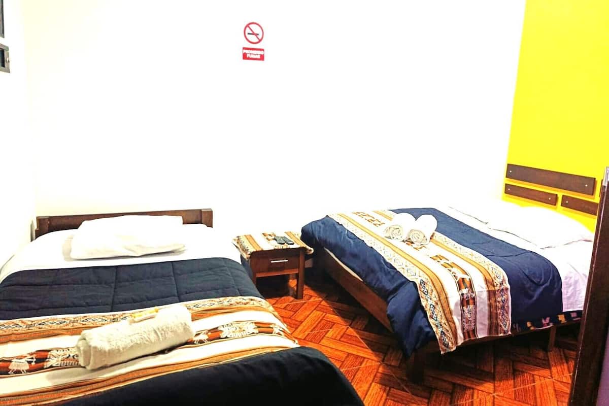 Une chambre d’hôtel avec deux lits, un plancher en bois, un mur jaune et un panneau indiquant qu’il est interdit de fumer.