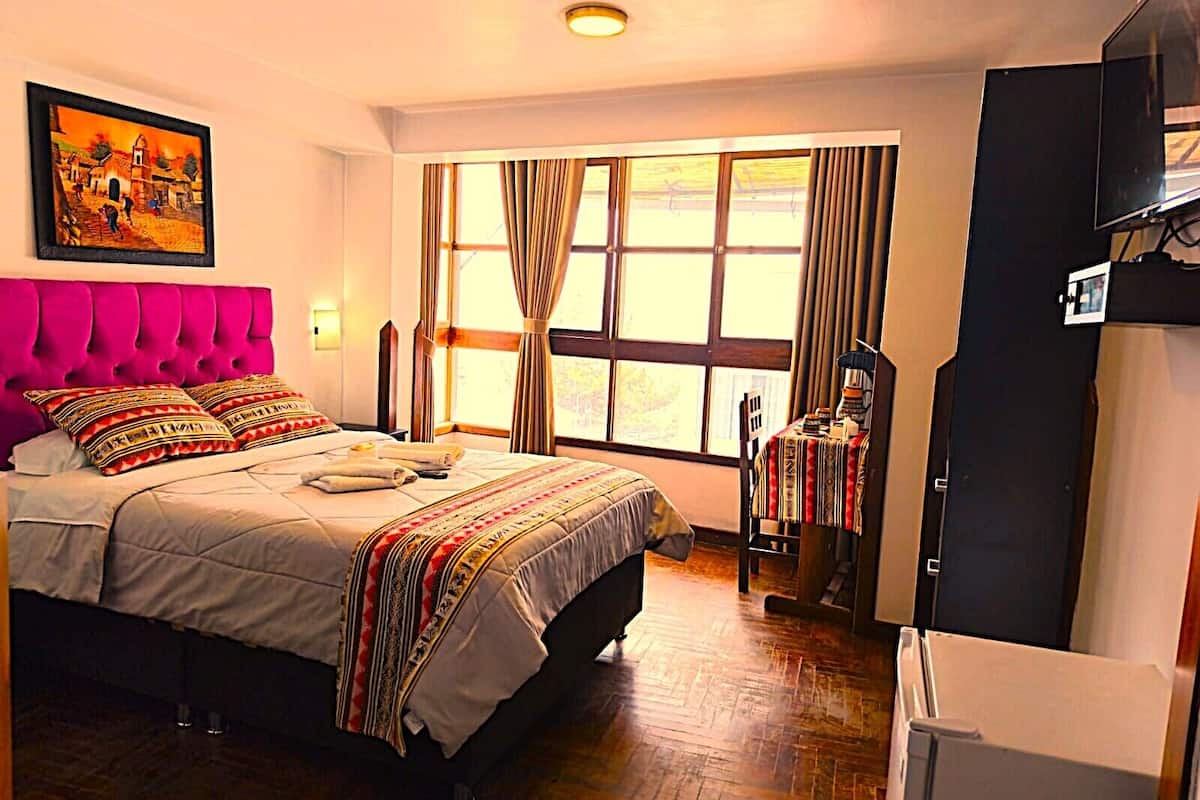 Une chambre à coucher avec un lit, un tableau, une fenêtre avec des rideaux et un bureau avec une chaise.