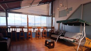 Ruime kamer met groot raam en uitzicht op de bergen, houten meubilair en een schommelstoel.