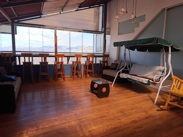 A spacious room with a large window offering a mountain view, wooden furniture, and a swing chair.