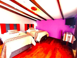 Une chambre avec deux lits, des poutres en bois, une tête de lit rouge et noire à rayures, un mur violet et un téléviseur.
