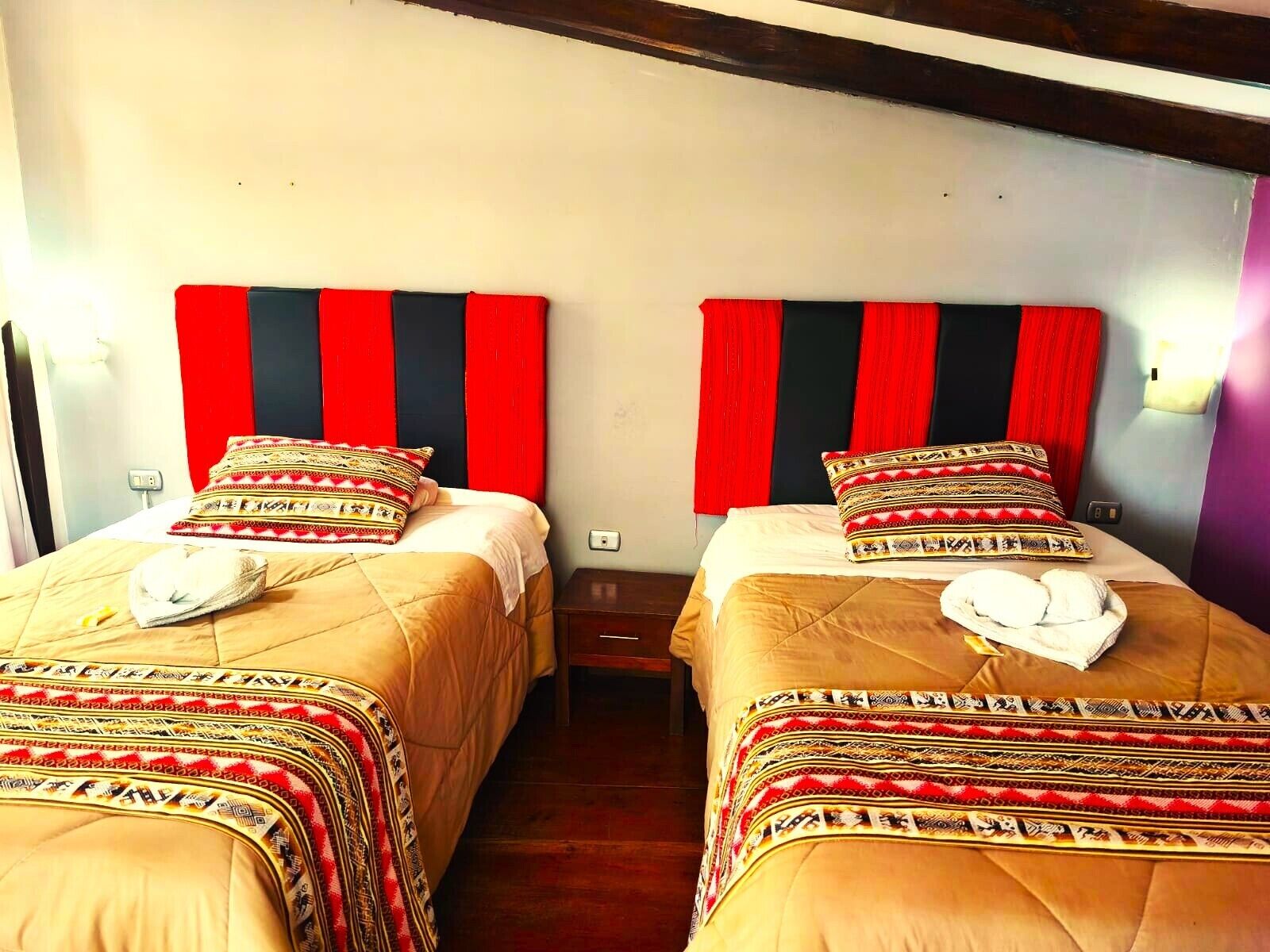 Une chambre avec deux lits, chacun recouvert d’une couvre-lit à motifs et agrémenté d’oreillers, et dotée d’une tête de lit rayée de rouge et de noir.