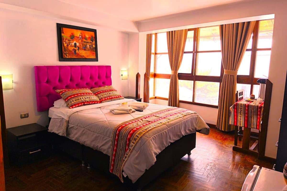 Une chambre d’hôtel avec un grand lit, un tableau au mur, une fenêtre avec des rideaux et une petite table recouverte d’une nappe.