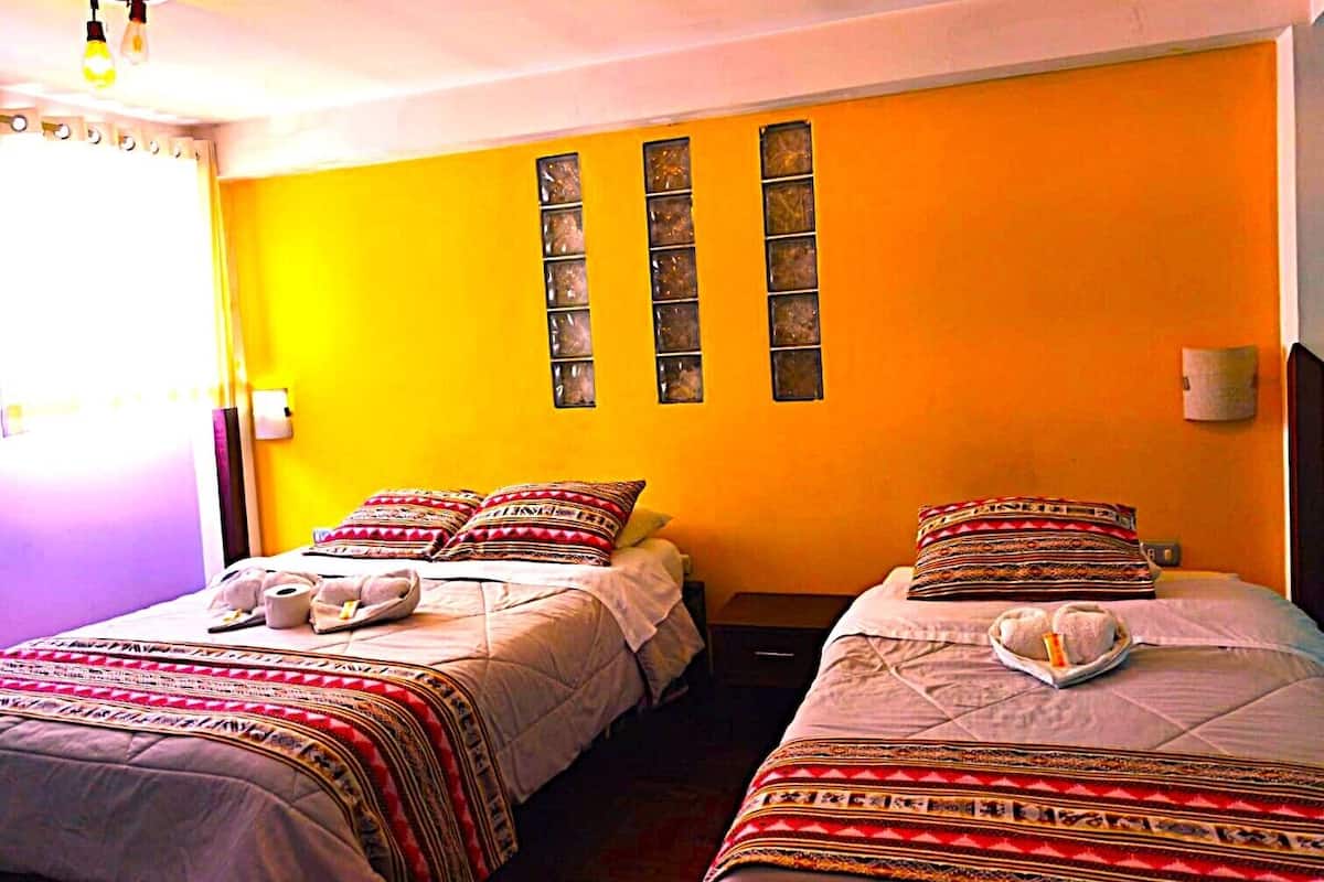 Une chambre avec deux lits, chacun agrémenté de draps et d’oreillers à motifs, une table de chevet avec une lampe et une fenêtre ornée de panneaux de verre décoratifs.
