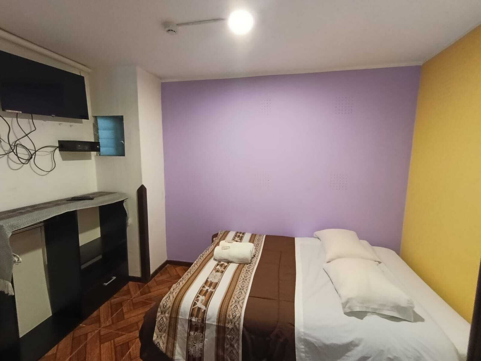 A small, simple room with a bed, a desk, and a television.