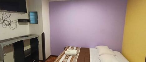 A small, simple room with a bed, a desk, and a television.