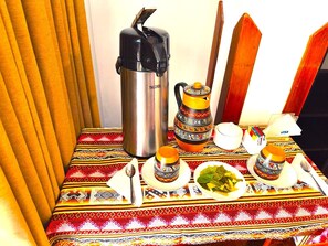 Une table avec un thermos, un pichet décoratif, des tasses, des assiettes remplies de nourriture et une cuillère.
