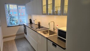 Una cocina moderna con armarios blancos, un lavamanos de acero inoxidable, un microondas integrado y una ventana con persianas.