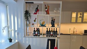 Un comedor moderno con una mesa blanca, sillas negras y una estantería para vinos con botellas.
