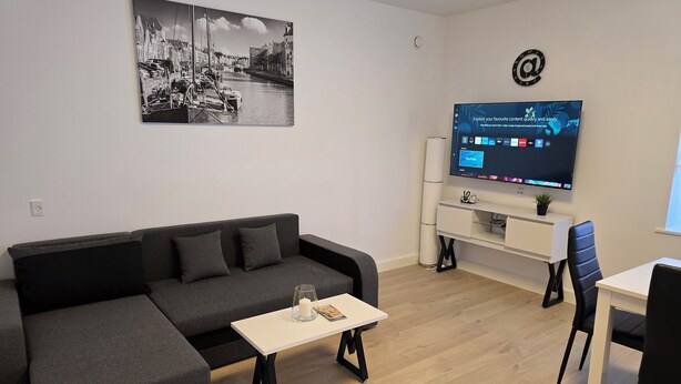 Una sala de estar moderna con un sofá seccional gris, una mesa de centro, un televisor sobre un mueble bajo y un escritorio pequeño con una silla.