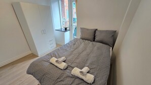 Un dormitorio con una cama, un armario, una ventana y una planta pequeña.