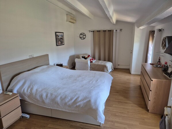 Una habitación de hotel con una cama grande, dos camas más pequeñas, un aparador, un espejo y un televisor montado en la pared.