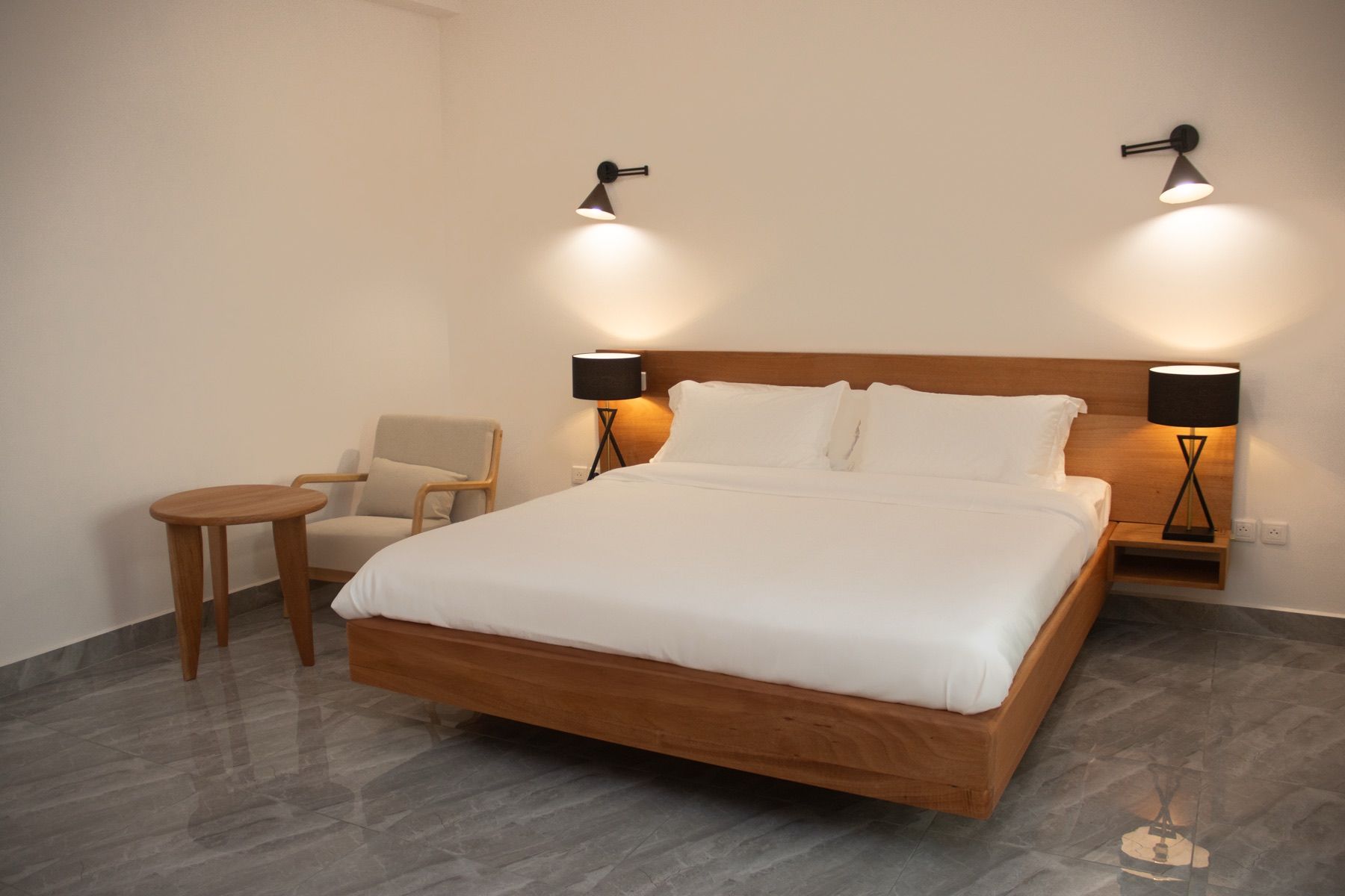 A hotel room with a wooden bed, two bedside lamps, a small round table, and a chair.