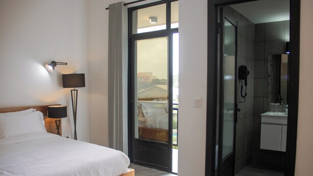 Una camera d'albergo con un letto, un comodino, una lampada, un bagno con doccia e vista all'esterno.