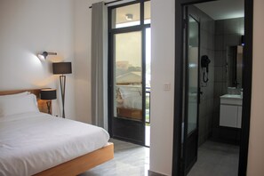 A hotel room with a bed, a nightstand, a lamp, a bathroom with a shower, and a view of the outside.