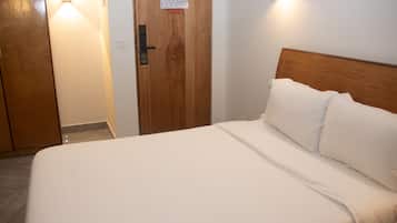 Une chambre d’hôtel avec une porte en bois, un lit avec une literie blanche et un luminaire fixé au mur.