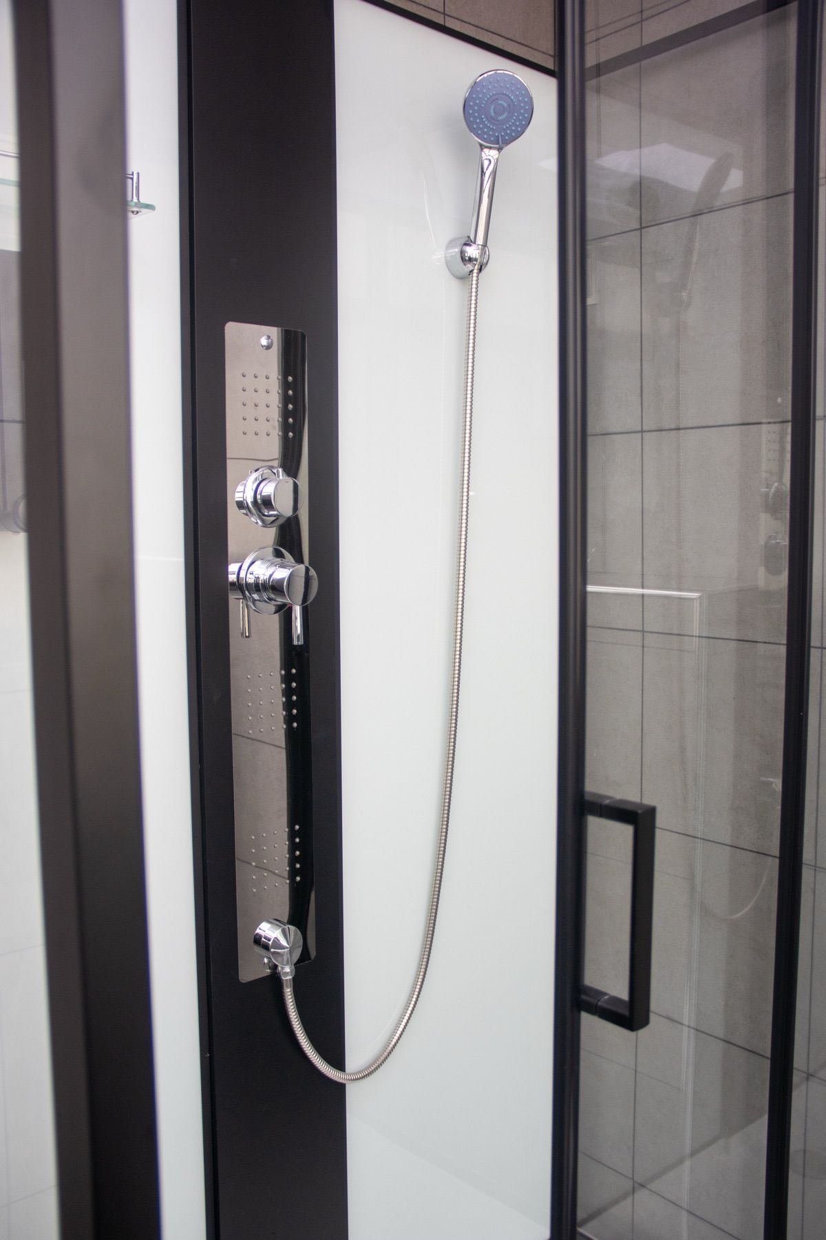 A shower with a handheld showerhead and a wall-mounted control panel.