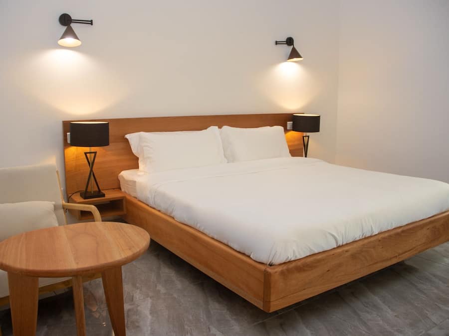A single-bed room with a wooden headboard, two bedside lamps, a small wooden table, and a white chair.