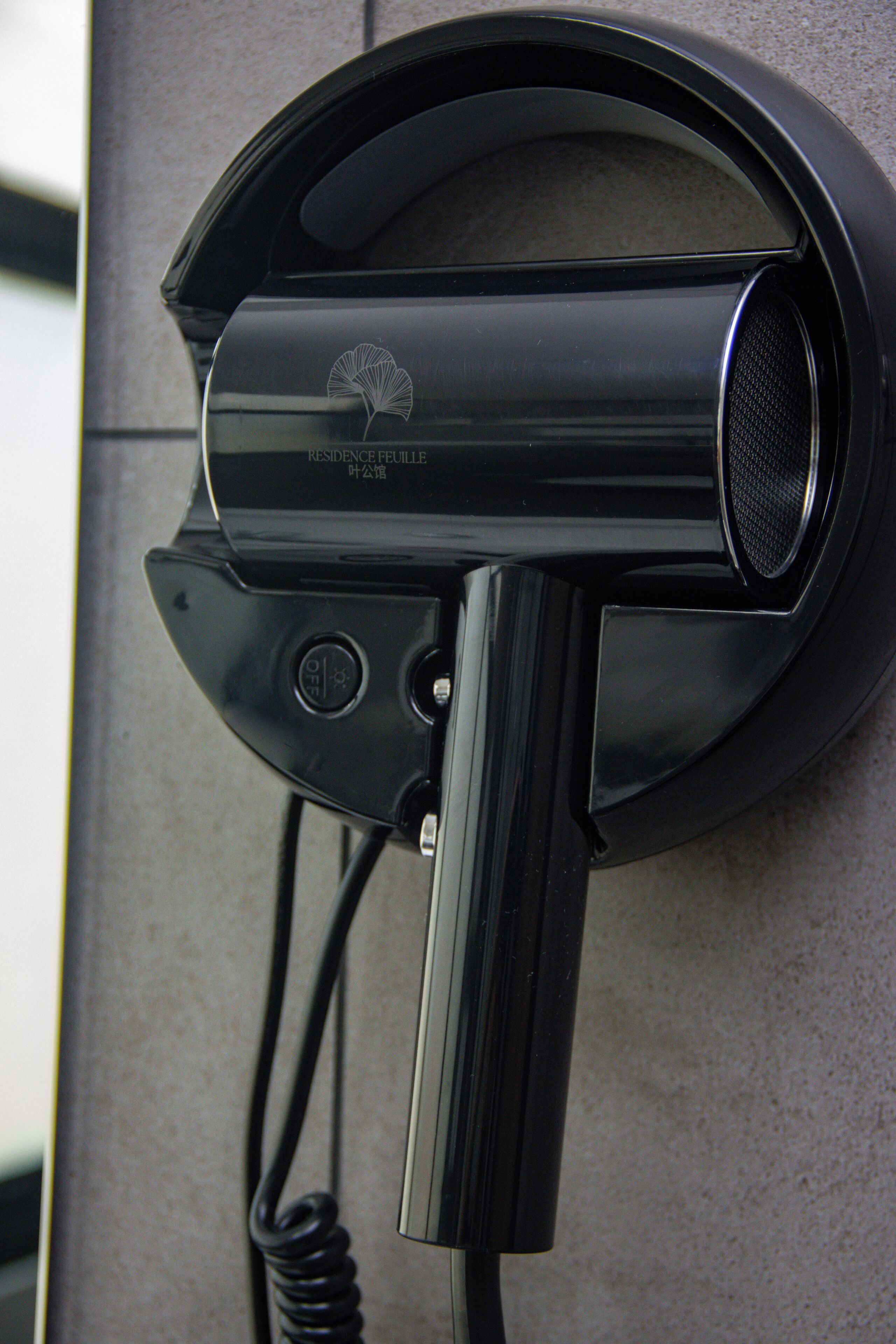 A black hair dryer mounted on a textured wall.