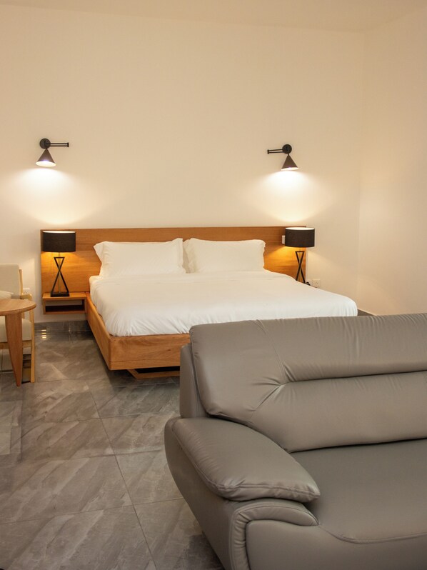 A hotel room with a bed, two bedside lamps, a wooden headboard, a grey sofa, and a small table.