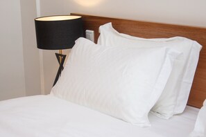 A neatly made bed with white linens and pillows, a black lamp with a gold base, and a wooden headboard. - Résidence Feuille (Pointe-Noire)