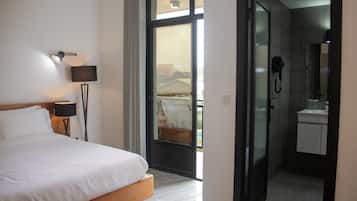 A hotel room with a bed, a lamp, a bathroom with a shower, and a view through a glass door.