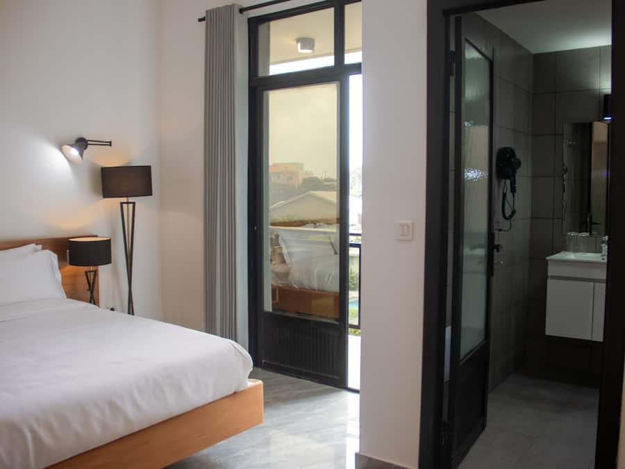 Ein Hotelzimmer mit einem Bett, einer Lampe, einem Badezimmer mit Dusche und Blick durch eine Glastür.