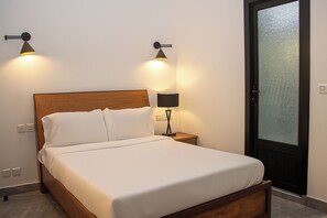 A neatly made bed with white linens, a wooden headboard, and two wall-mounted lamps on either side.