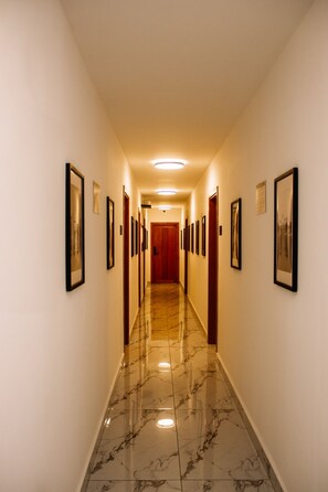 A hotel hallway with framed pictures on the walls, a marble floor, and a wooden door at the end. - Résidence Feuille  (Pointe-Noire)
