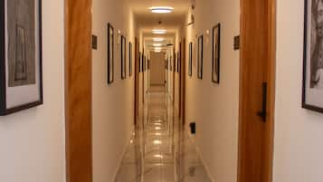 Corredor de hotel com portas de madeira, quadros nas paredes e piso de mármore.