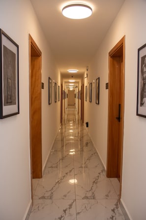 A hotel hallway with wooden doors, framed pictures on the walls, and a marble floor. - Résidence Feuille  (Pointe-Noire)