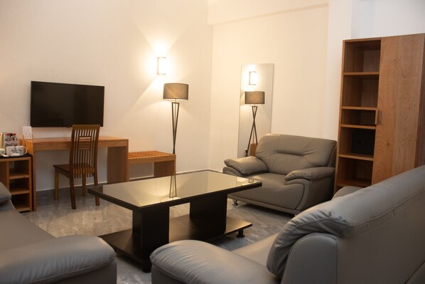 A modern living room with a flat-screen TV, a sofa, a coffee table, and two floor lamps. - Résidence Feuille (Pointe-Noire)