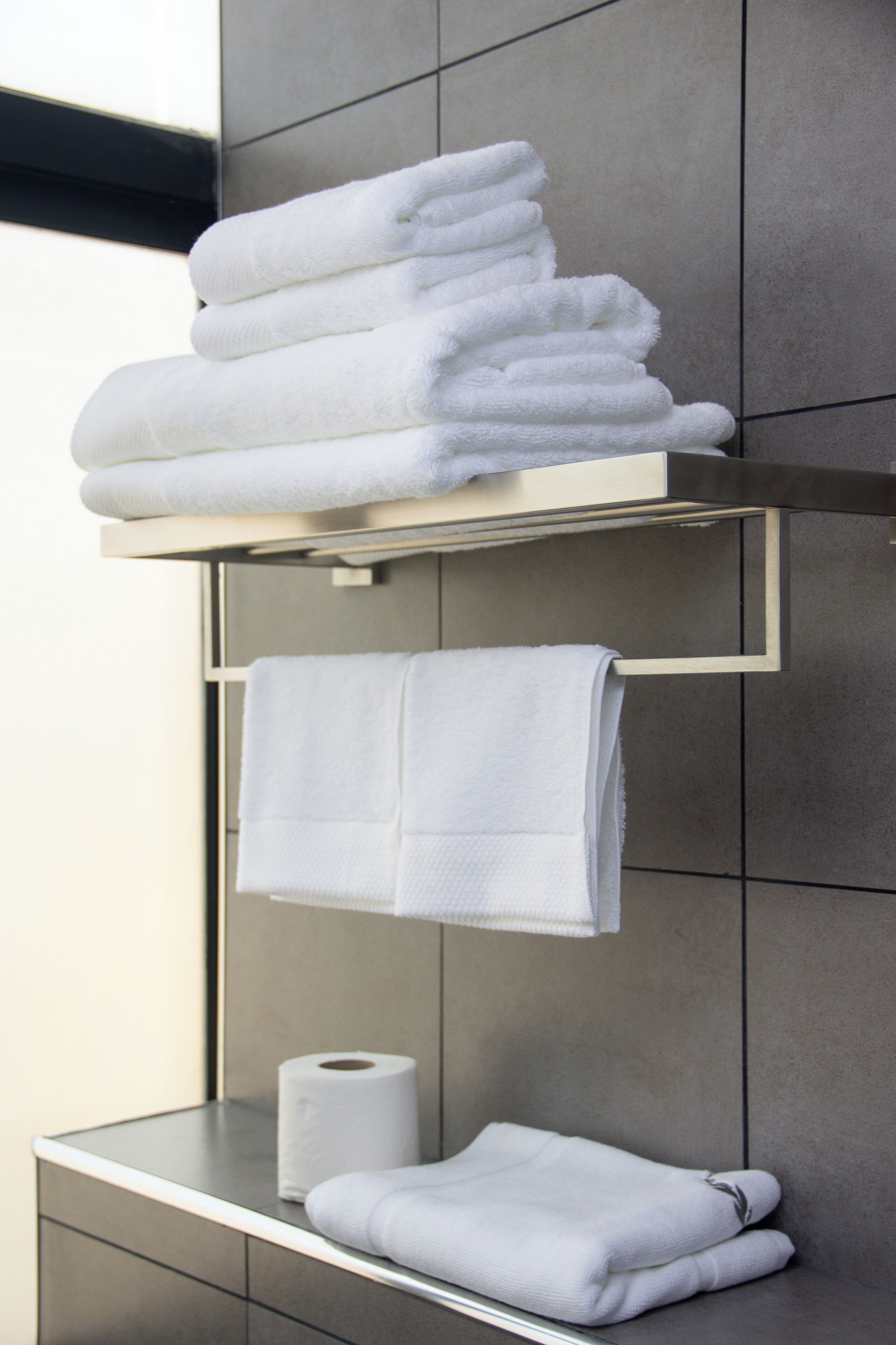 A bathroom with a towel rack holding neatly folded towels, a roll of toilet paper, and a mirror.