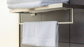 A bathroom with a towel rack holding neatly folded towels, a roll of toilet paper, and a mirror.