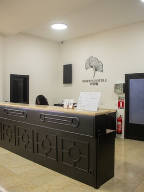 A reception desk with a sign above it, a fire extinguisher, and a door in the background. - Résidence Feuille (Pointe-Noire)
