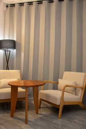 A room with a striped curtain, a round wooden table, two beige armchairs, and a floor lamp. - Résidence Feuille (Pointe-Noire)