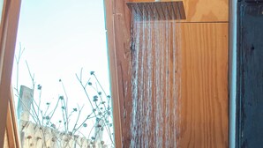 A bathroom with a wooden shower enclosure, a visible window, and a view of the outside.