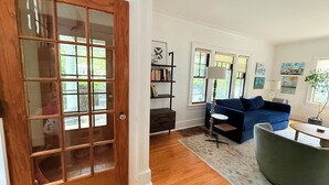 Un salon avec une porte en bois, un canapé bleu, une petite table et une bibliothèque.