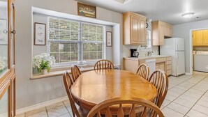 A kitchen with a dining table, chairs, a refrigerator, and a window with blinds. - Slab Road Hill Country Escape! (Llano County)