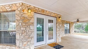 A covered porch with stone walls, a door with a glass panel, and a ceiling fan. - Slab Road Hill Country Escape! (Llano County)
