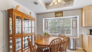A dining room with a wooden table and chairs, a glass-fronted cabinet, and a window with blinds. - Slab Road Hill Country Escape! (Llano County)